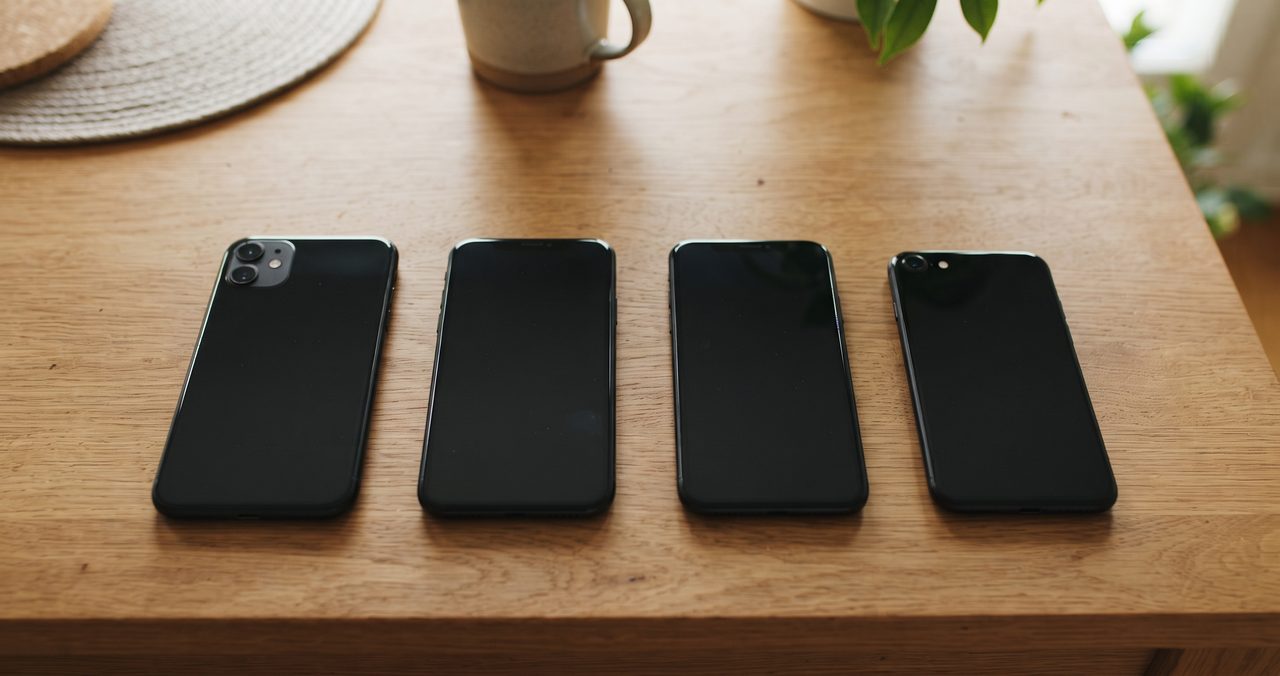 木製テーブルの上に家族4人分と思われるスマートフォンが画面オフの状態で並べて置かれた真上からの俯瞰ショット