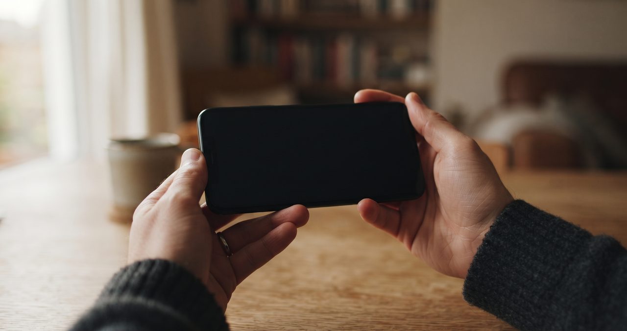 スマートフォンを横向きに持ち、動画再生を連想させる暗い画面を見つめている手元のクローズアップ
