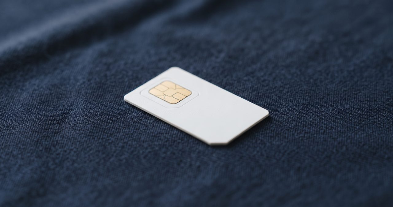 ネイビーブルーの布地の上に金色のIC接点面を見せて斜めに置かれた無地の白いSIMカード